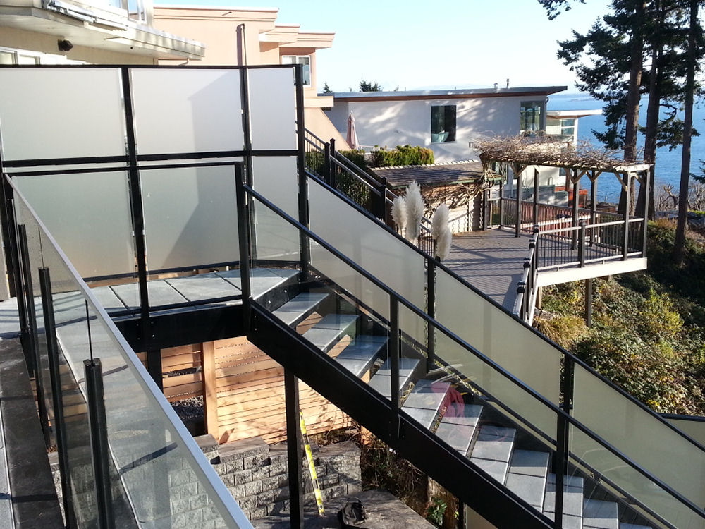 A multi-story building features glass railings and terraces with an ocean view. A staircase leads down to a wooden pergola and landscaped garden.