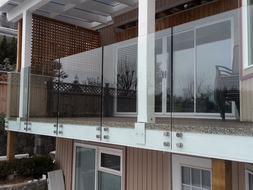 Glass balcony railing on a modern wooden house with sliding doors and outdoor seating.
