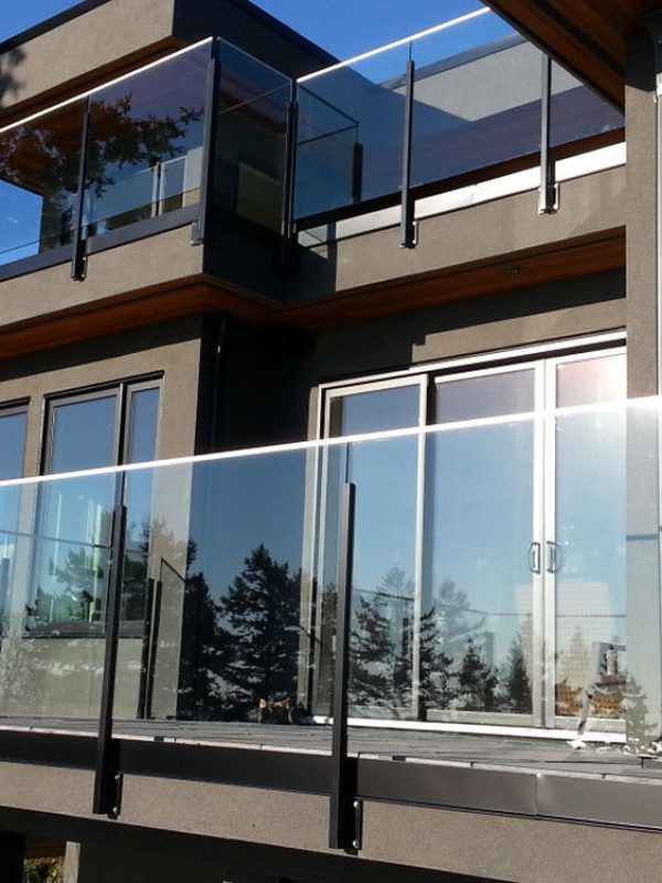 Modern building exterior with large glass-paneled balconies, reflecting trees and a clear blue sky.